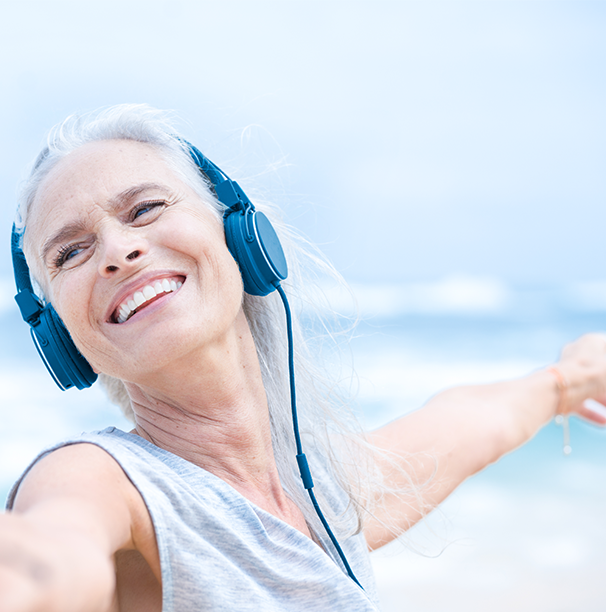 Skin Health Glad kvinna som lyssnar på musik vid havet och sträcker ut sina armar.