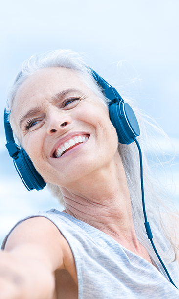 Glad kvinna som lyssnar på musik vid havet och sträcker ut sina armar.